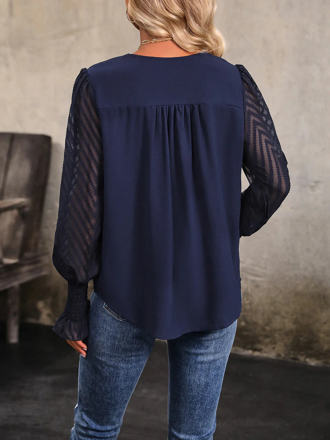 Woman wearing navy blouse with sheer lace long sleeves and blue jeans, standing indoors