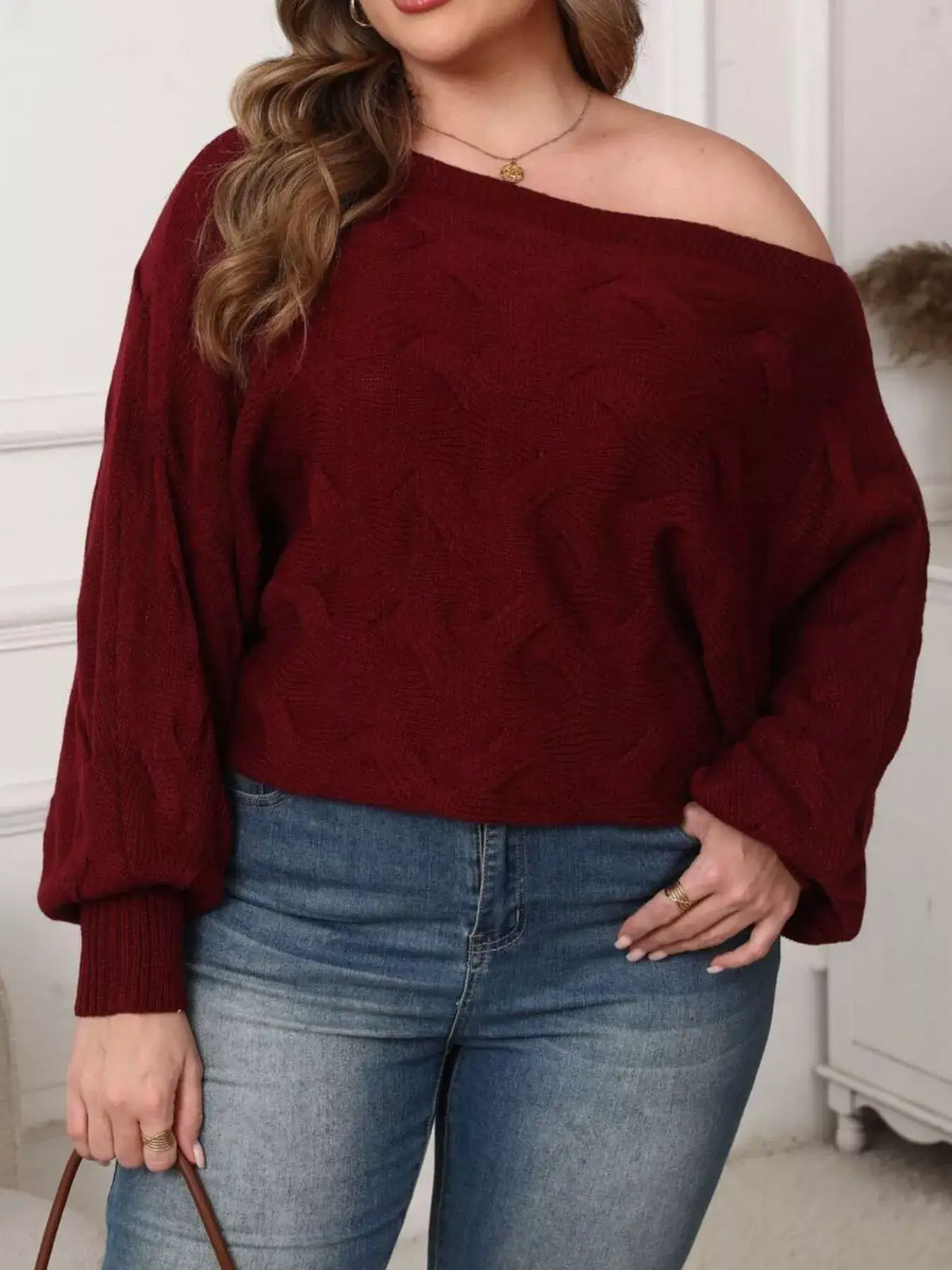 Plus size burgundy off-shoulder long sleeve sweater by Evie's Dreamland paired with blue jeans.
