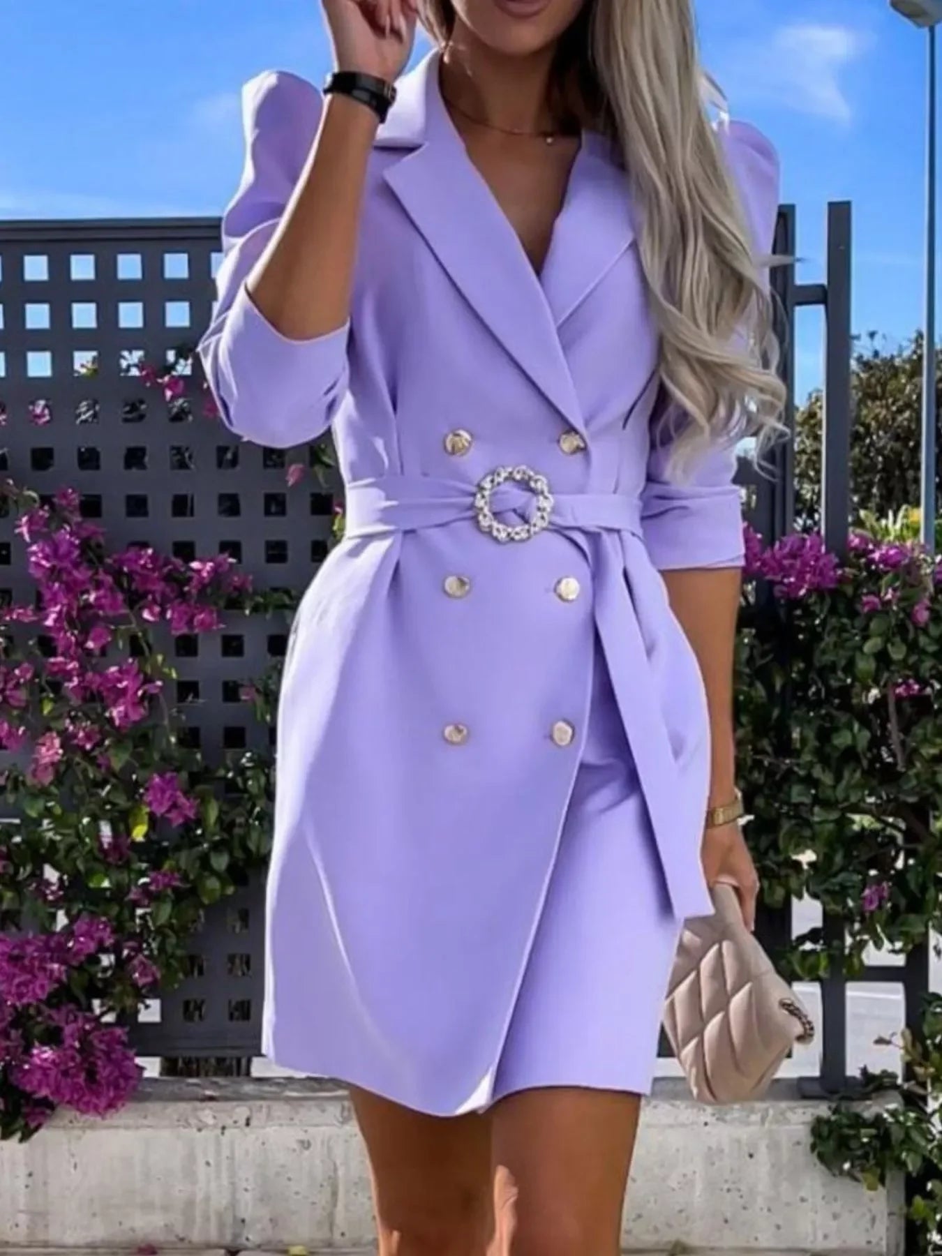 Woman in a lilac double-breasted blazer dress with gold buttons and belt outdoors with flowers