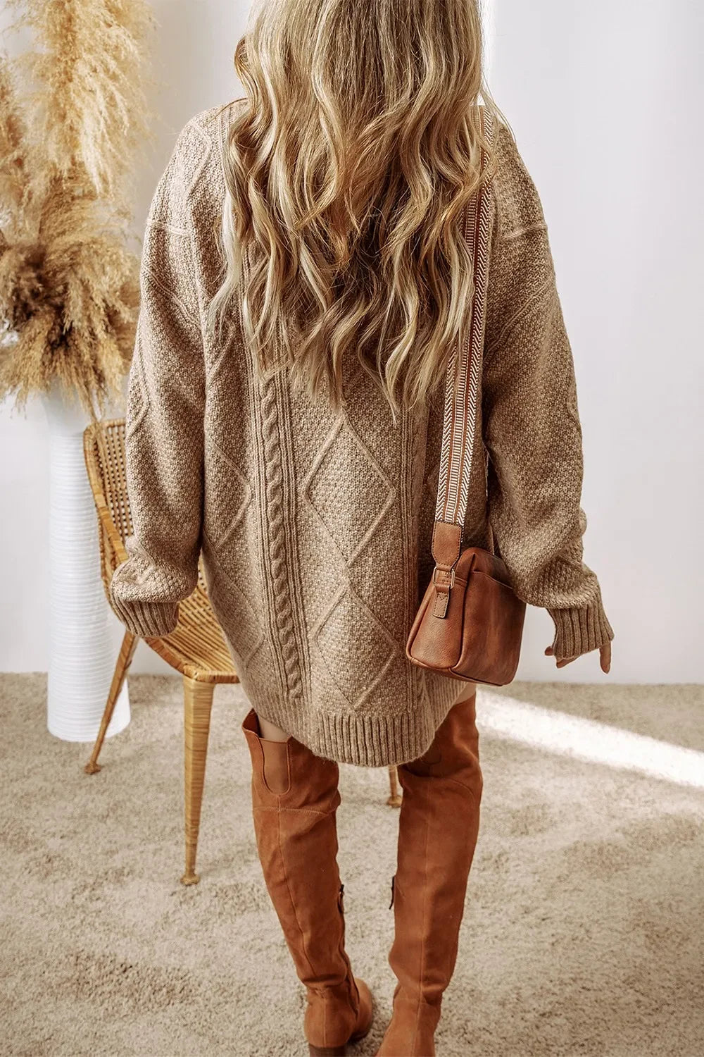 Woman in beige cable knit sweater dress with thigh-high brown suede boots and brown leather crossbody bag