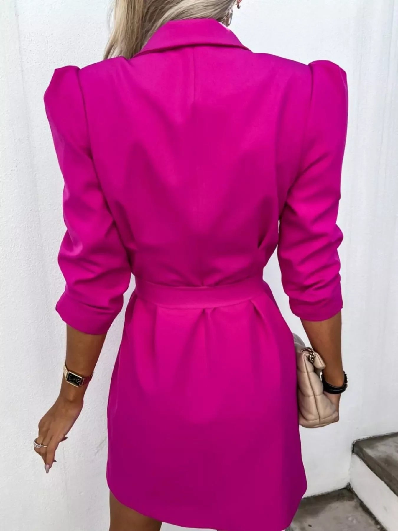 Back view of woman wearing vibrant magenta blazer dress with puffed shoulders holding beige handbag