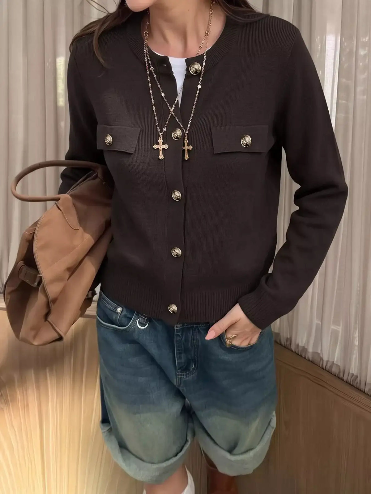 Woman wearing a dark brown Evie's Dreamland long sleeve knit button down cardigan with gold buttons and blue jeans.