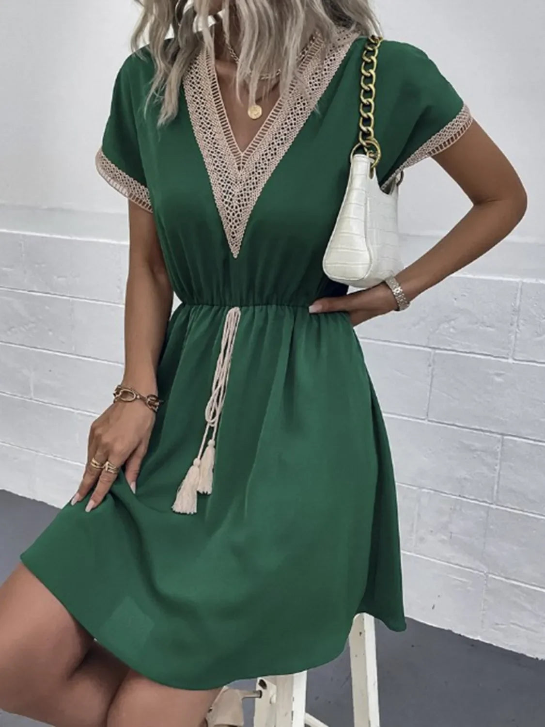 Green V-neck dress with lace trim and tassels, paired with white chain bag for chic everyday elegance