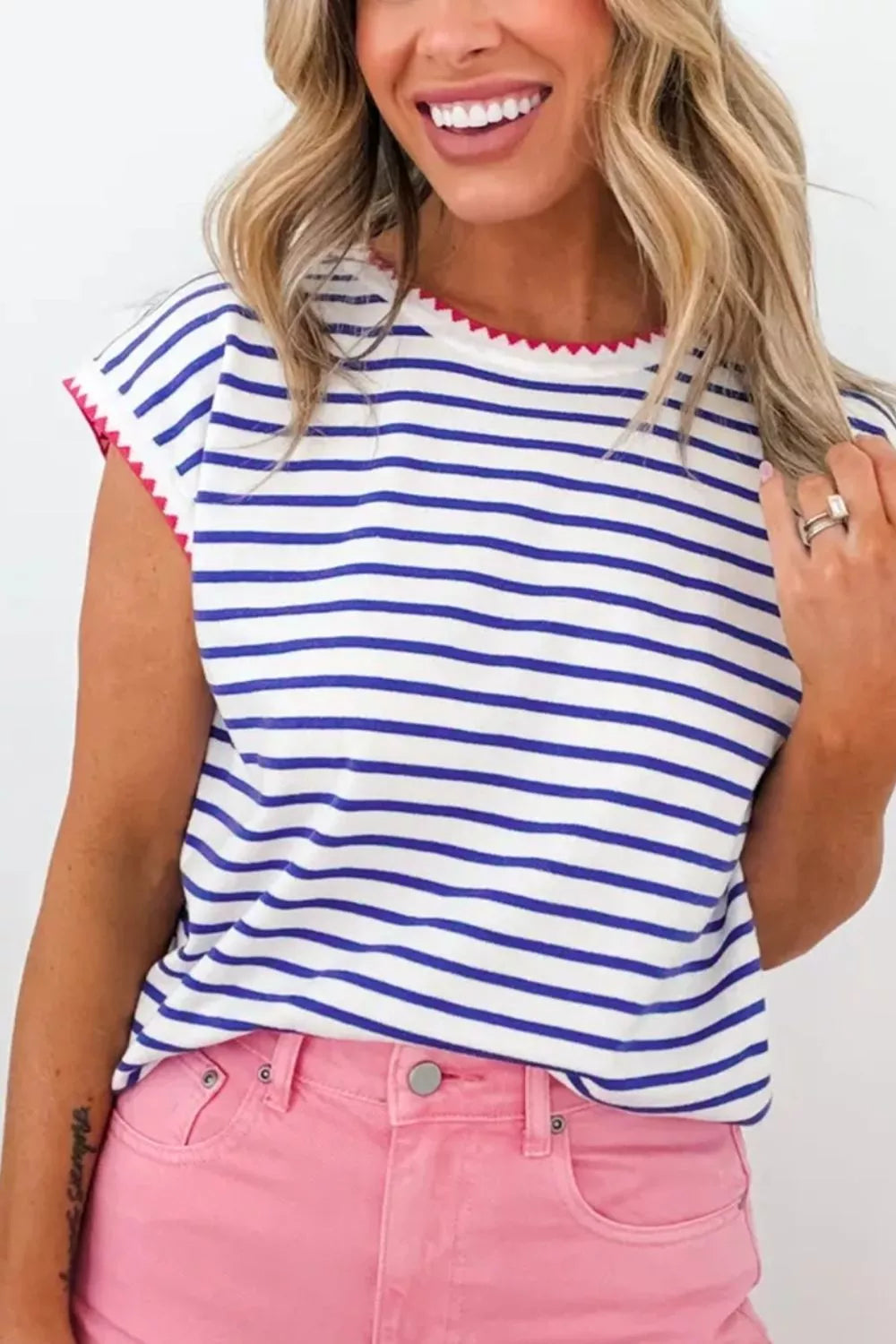 Blue and white striped sleeveless top with red trim, paired with pink jeans for a chic casual look.