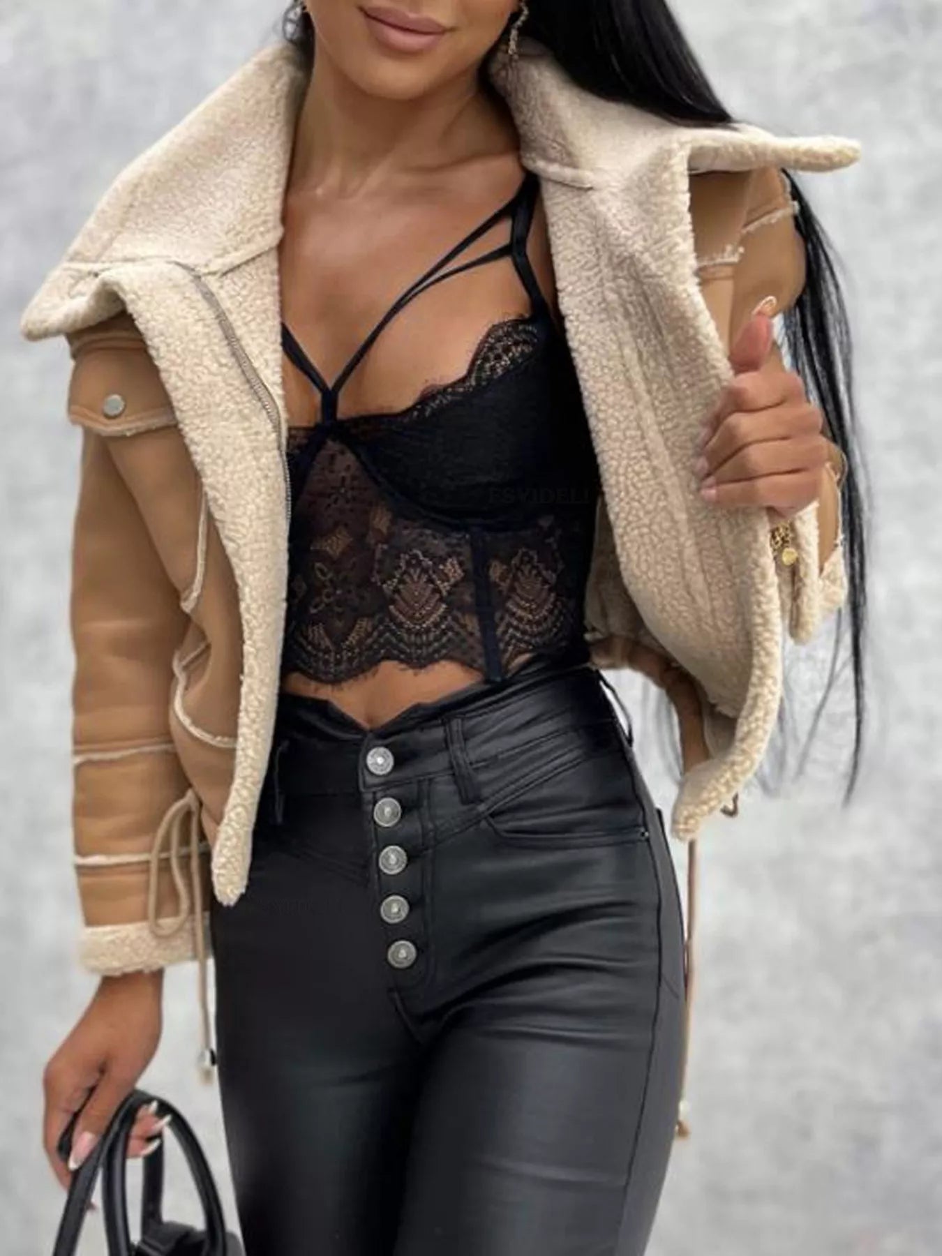 Woman wearing tan shearling jacket, black lace crop top, and high-waisted black leather pants with silver buttons