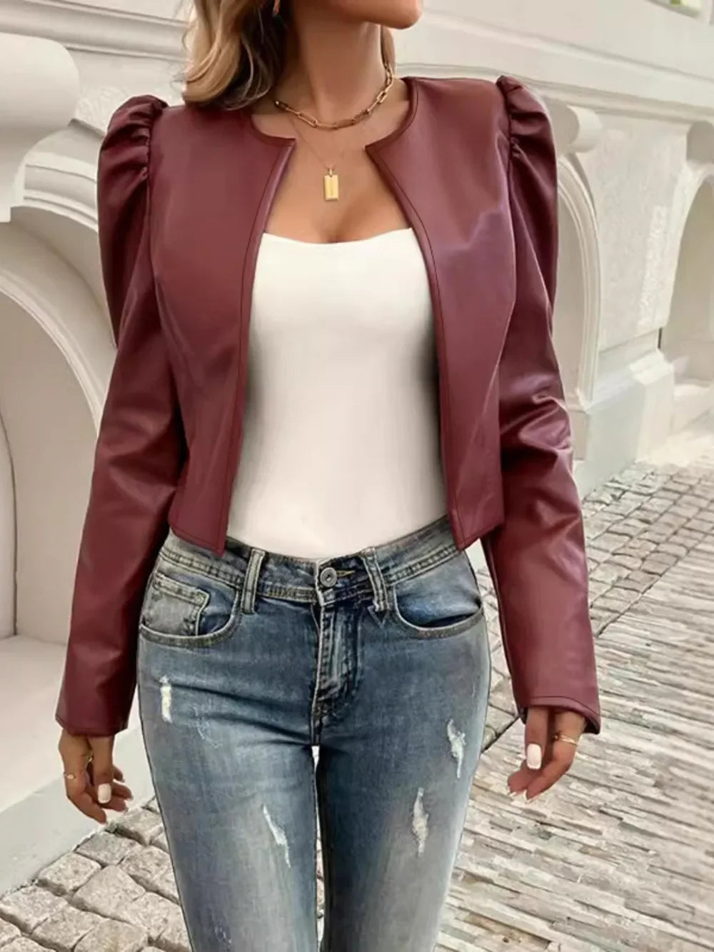 Woman wearing a burgundy faux leather cropped jacket with puff sleeves and blue jeans.