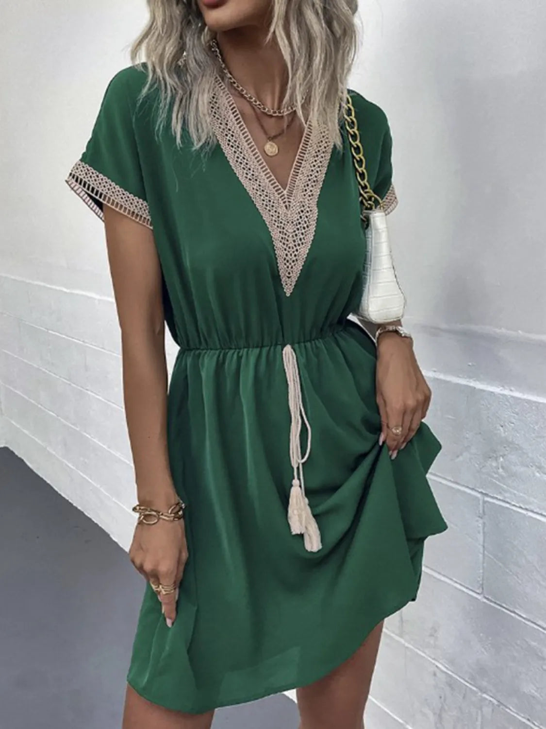 Green V-neck dress with lace trim and tassel drawstring, paired with gold accessories and white handbag