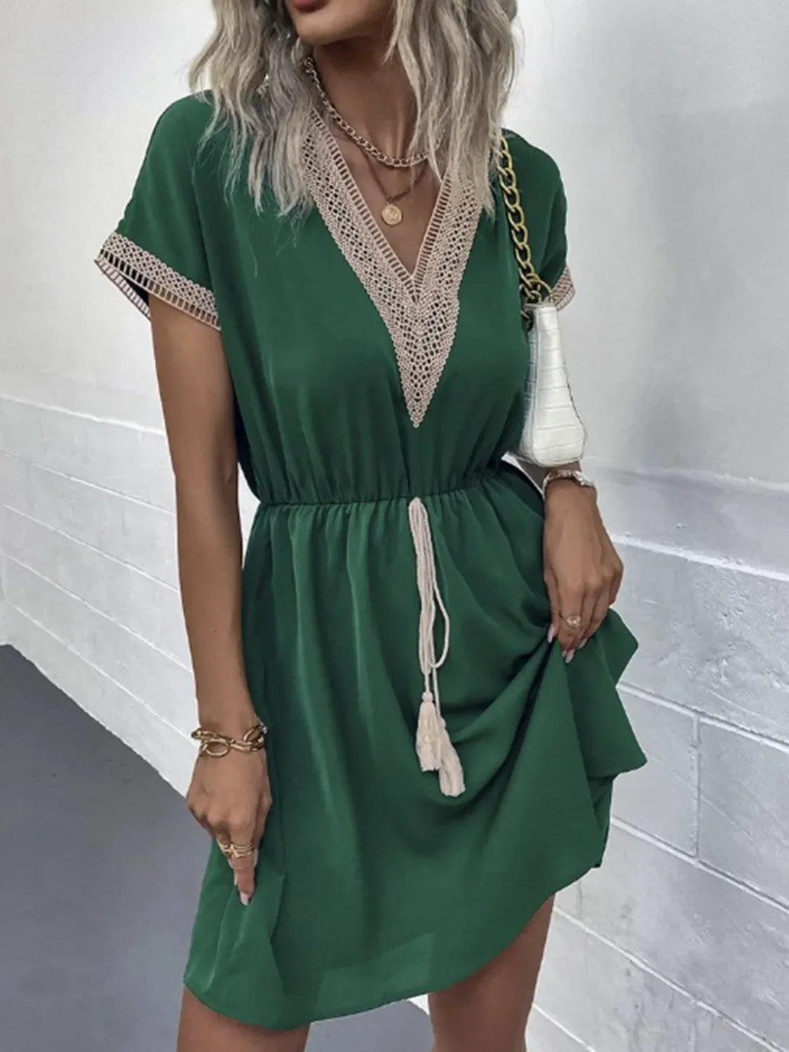 Green V-neck dress with lace trim and tassel drawstring, paired with gold accessories and white handbag