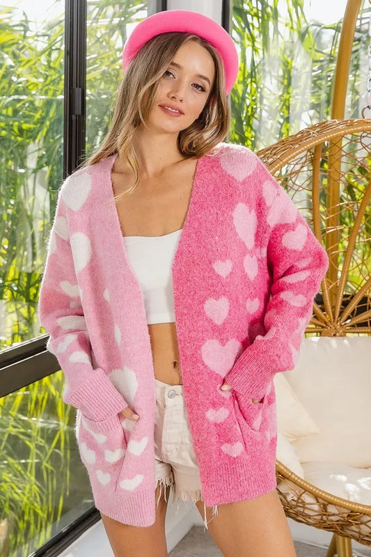 Woman wearing pink and white heart-patterned cardigan with white crop top and beige shorts indoors