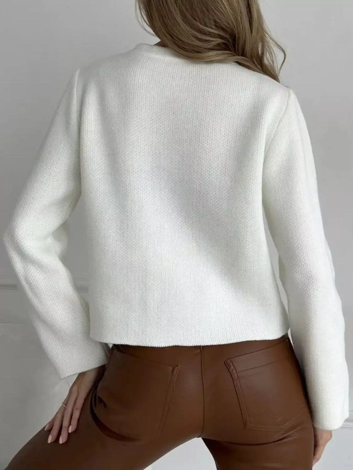 Back view of a white crew neck button down cardigan by Evie's Dreamland paired with brown leather pants.