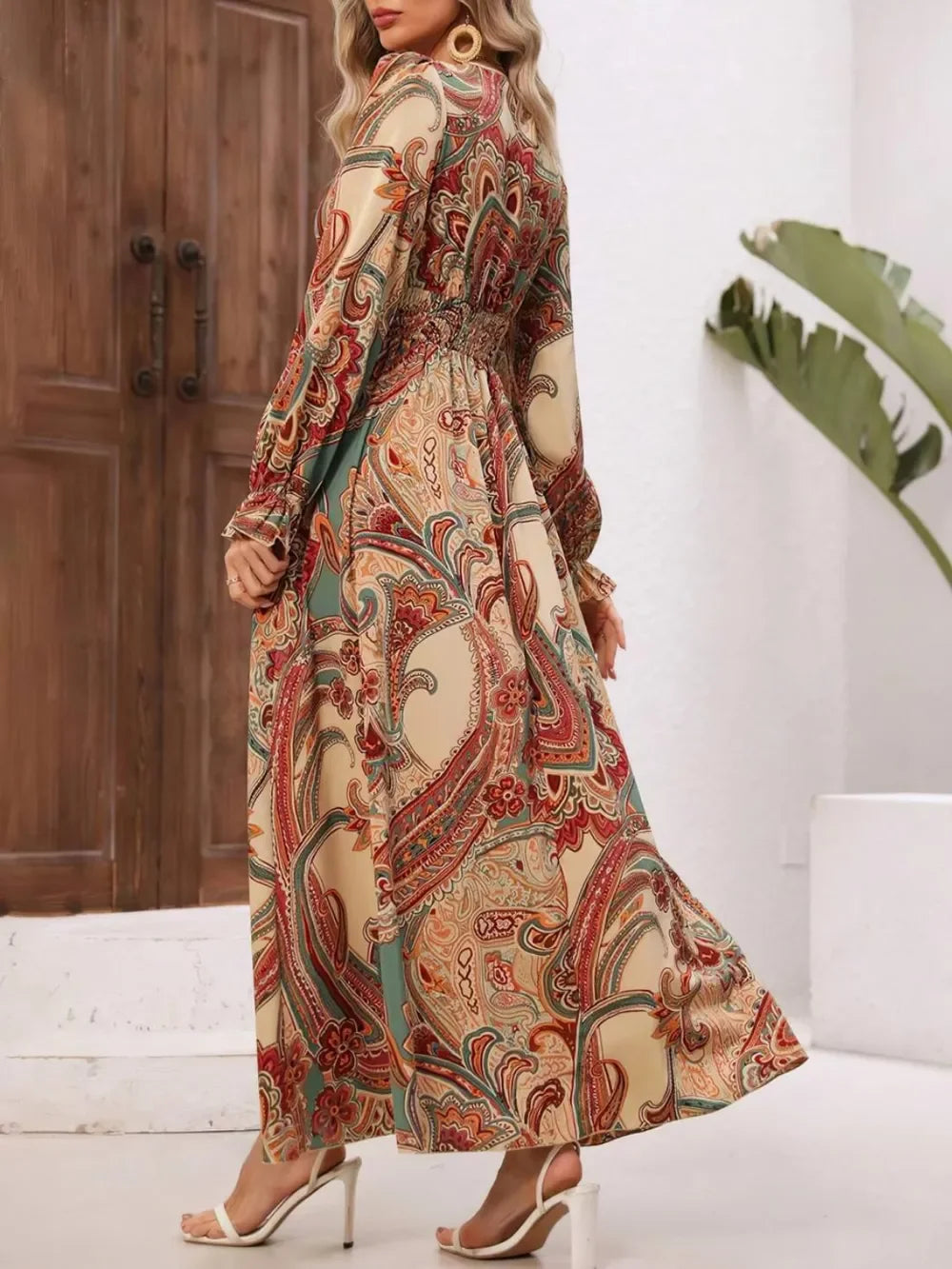 Woman wearing long-sleeve maxi dress with colorful paisley print in neutral indoor setting