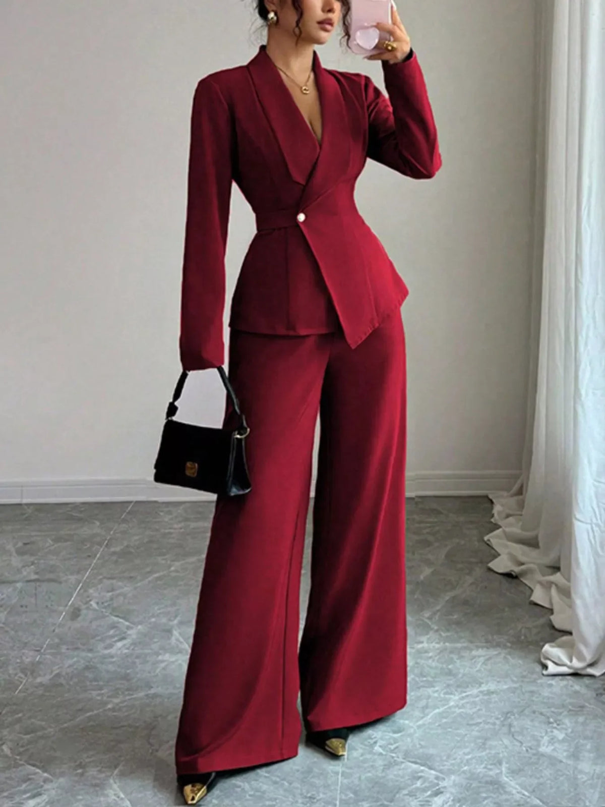 Woman in a stylish burgundy pantsuit with wide-leg trousers and blazer, holding a black purse