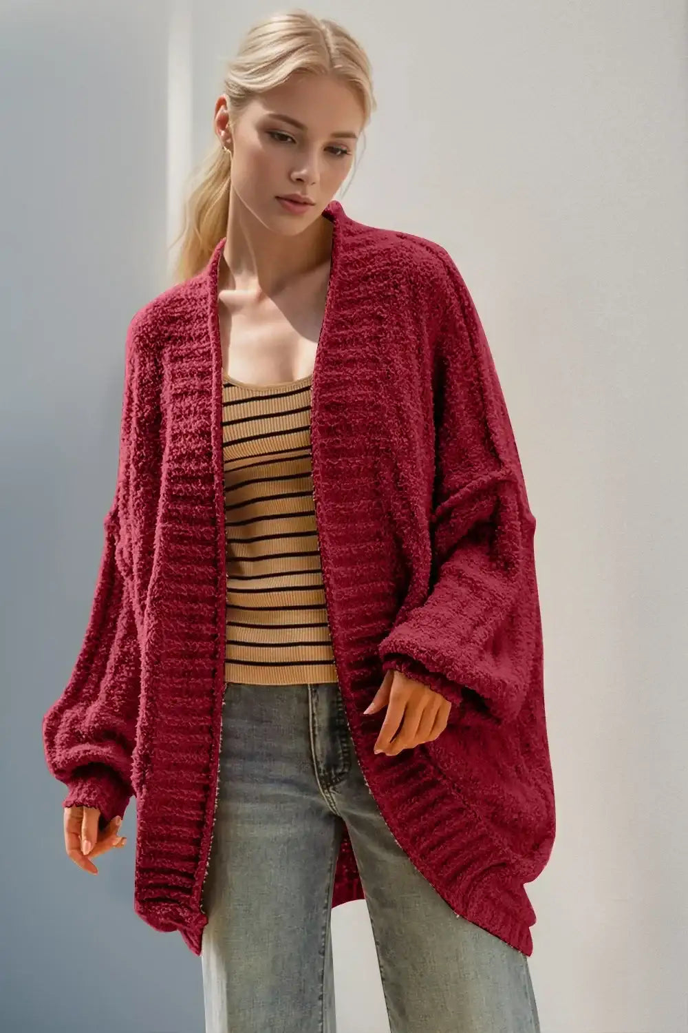 Woman wearing oversized cozy red cardigan, striped knit tank, and relaxed jeans