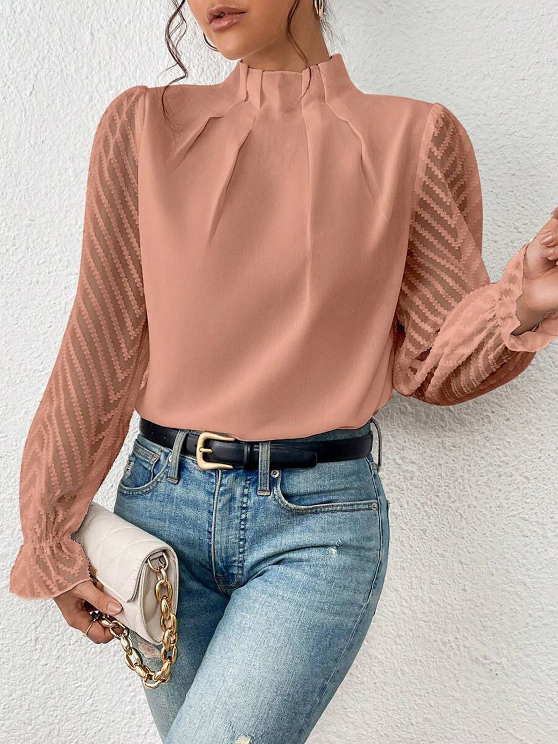 Woman wearing a pink chiffon blouse with sheer chevron sleeves, blue jeans, and a white purse