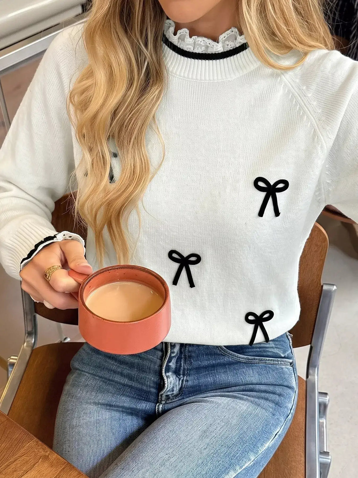 Woman wearing a white Evie's Dreamland sweater with black bow embellishments and lace trim neckline.