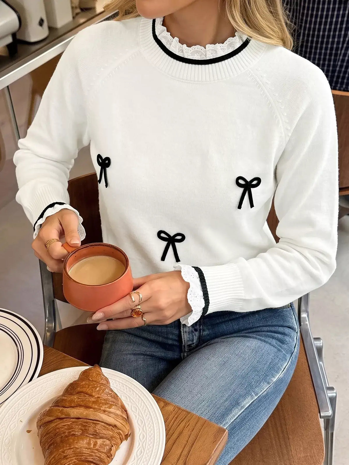 Woman wearing a white Evie's Dreamland bow-embellished sweater with lace trim and blue jeans.