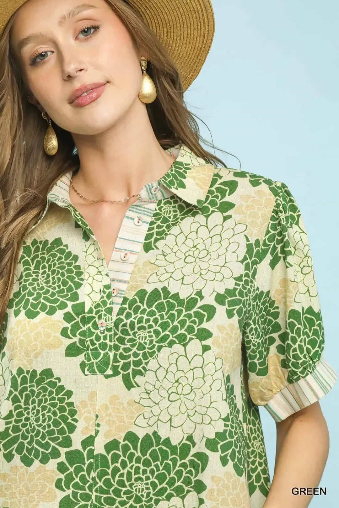 Woman in a green floral print blouse with puff sleeves and a straw hat