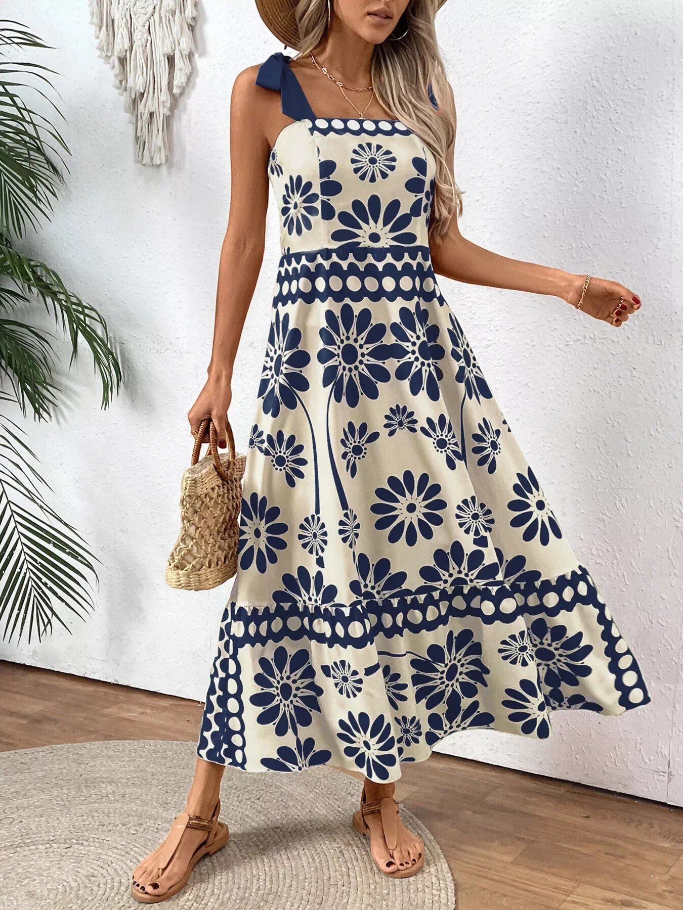 Blue floral midi dress with bow straps, paired with straw bag and sandals for summer elegance.
