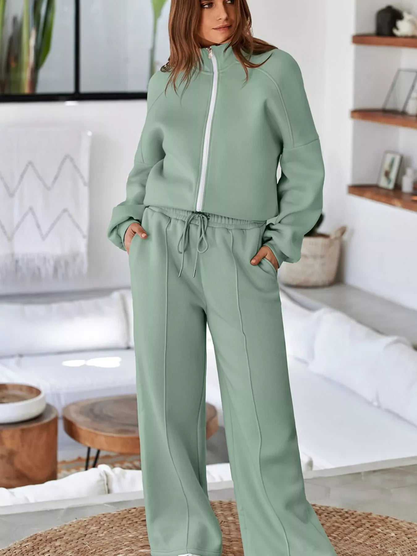 Woman wearing sage green zip-up sweatshirt and matching wide-leg sweatpants in modern living room