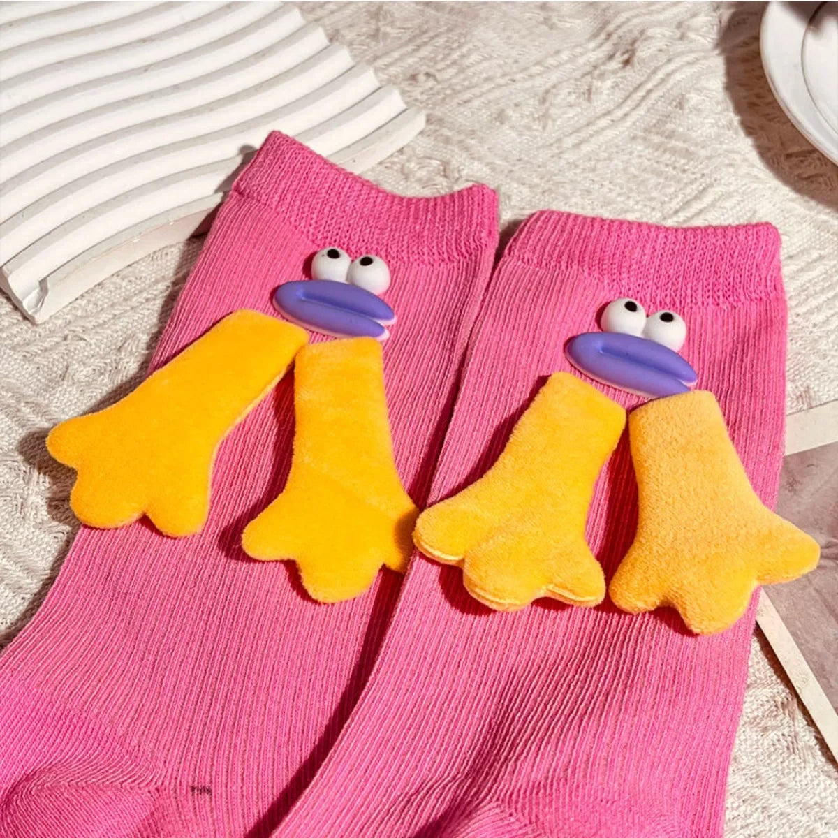 Pink socks with yellow duck feet and cartoon eyes design on a knitted fabric surface
