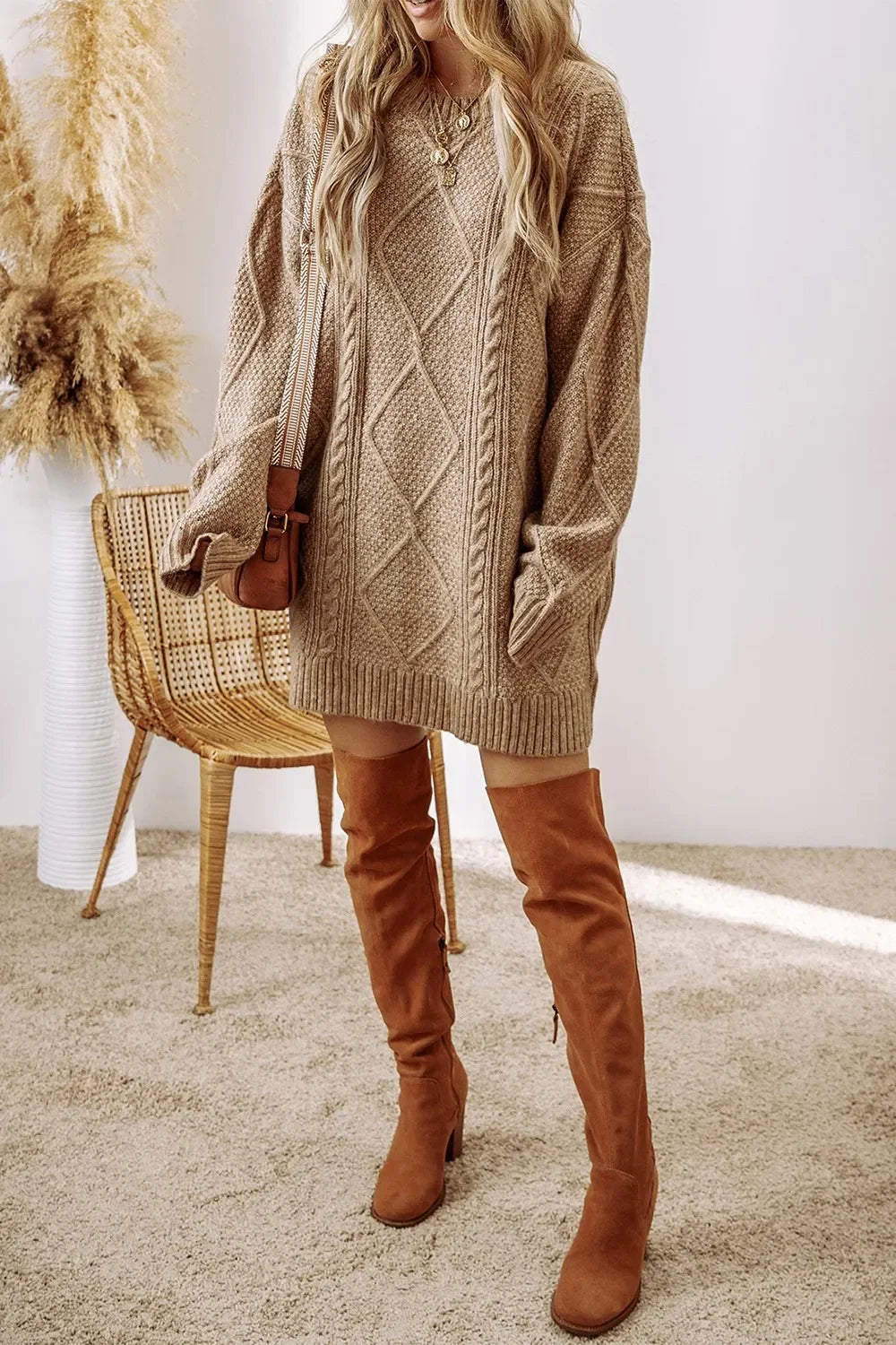 Woman wearing beige cable knit sweater dress with brown over-the-knee suede boots and layered gold necklaces