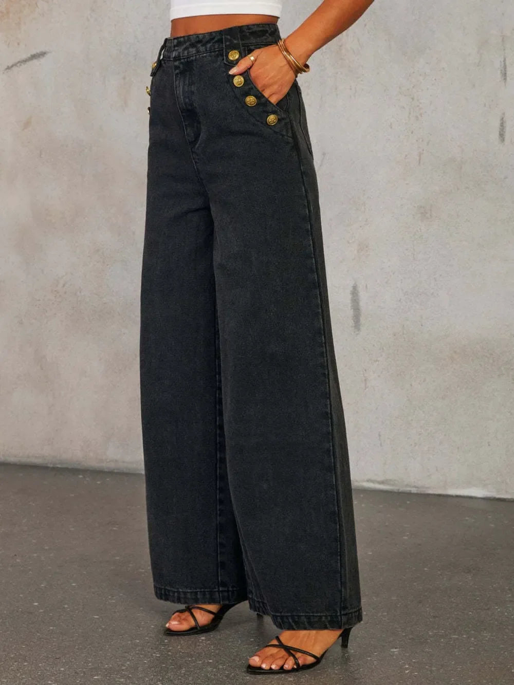Women's black wide-leg jeans with gold button details and high waist, styled with heels.