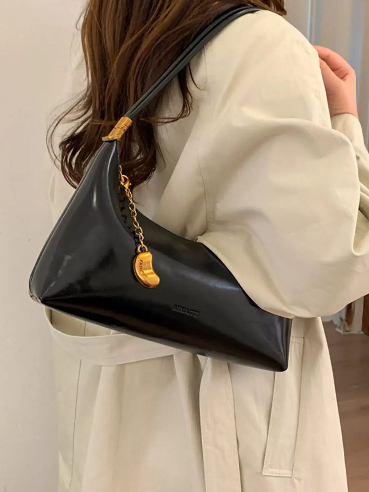 Evie's Dreamland black PU leather shoulder bag with a gold chain charm, paired with a cream coat.