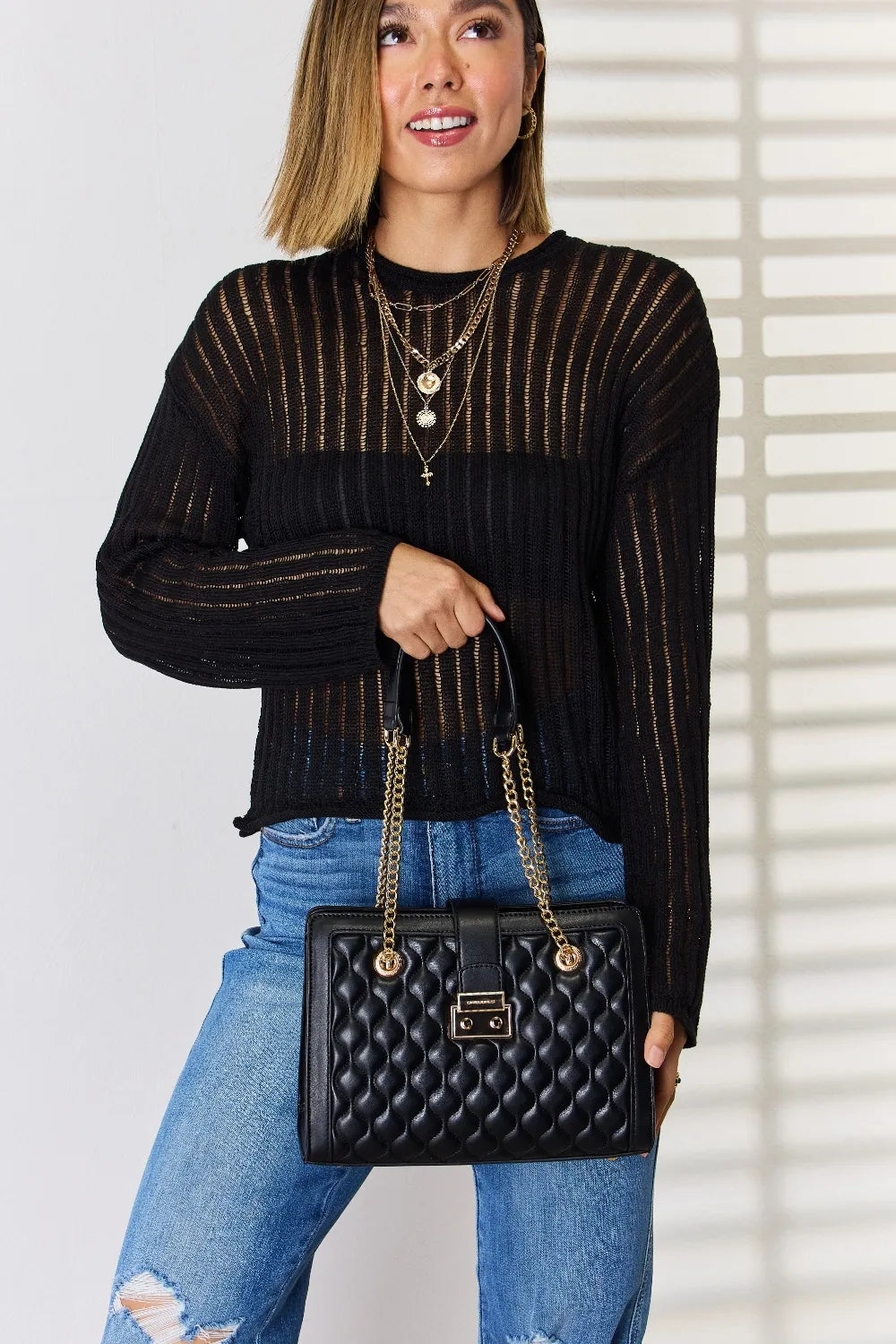 Woman wearing black sheer sweater and ripped jeans holding quilted black handbag with gold chain