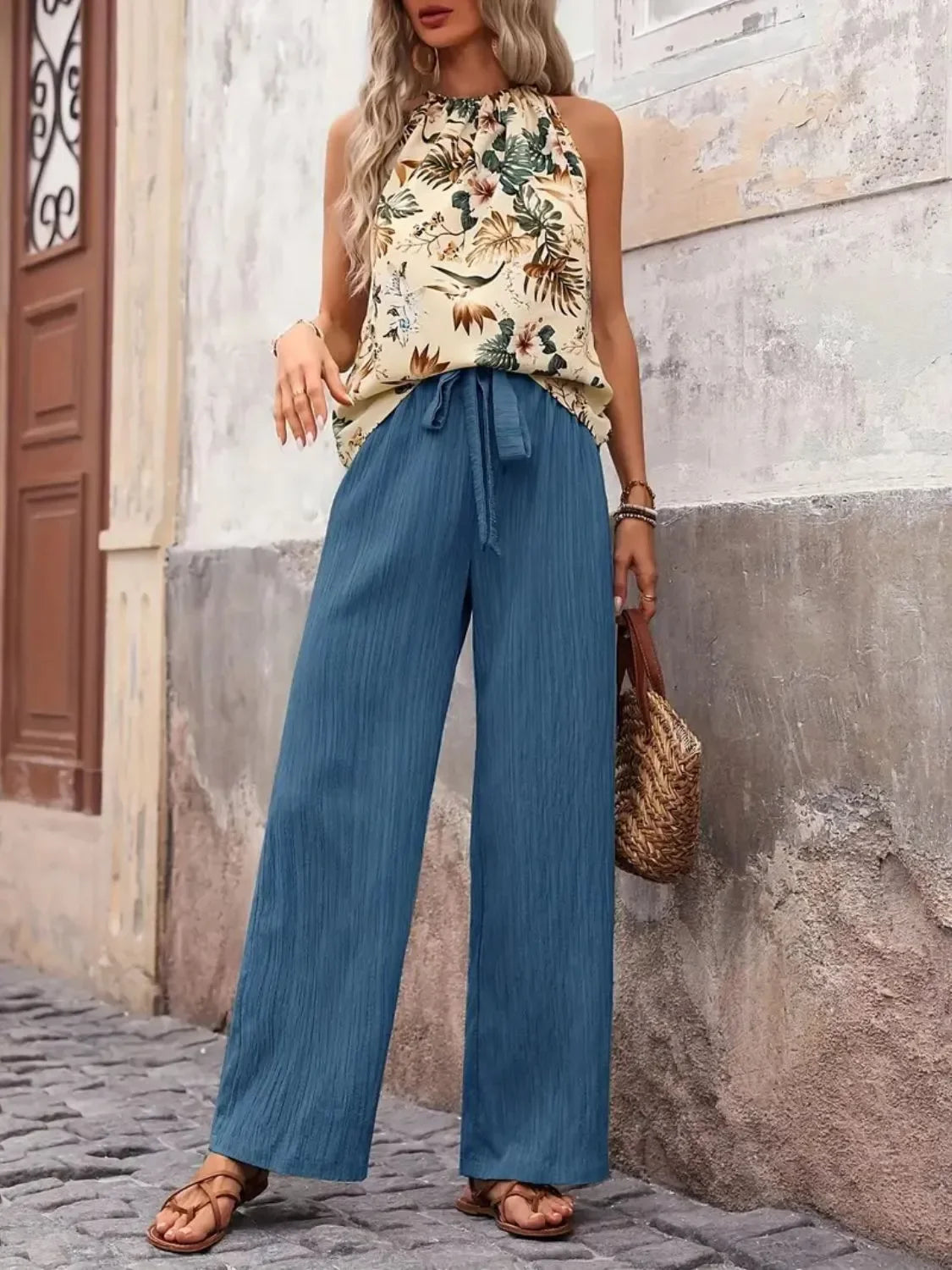 Woman wearing sleeveless floral top and wide-leg blue pants with sandals outdoors