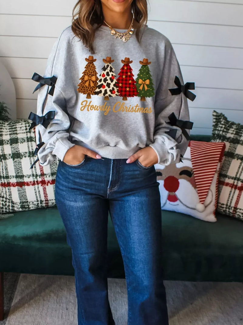 Woman sitting on a blanket under a golden autumn tree, wearing a soft and cozy 'Howdy Christmas' crewneck sweater.