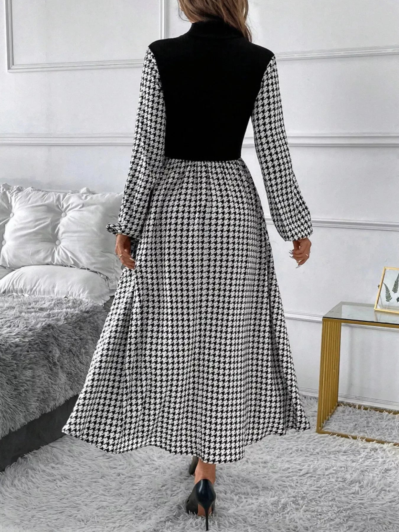 Woman wearing a black and white houndstooth long sleeve maxi dress with black high heels in a modern room