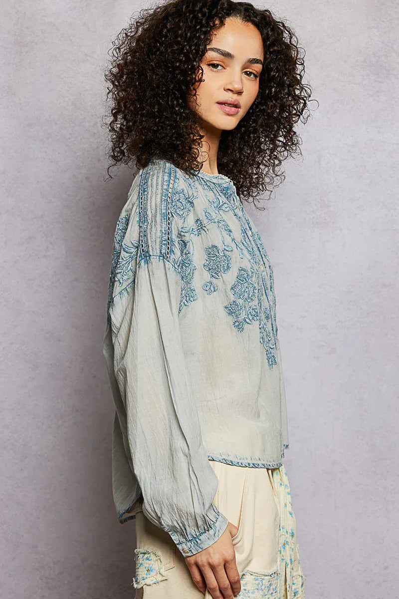 Woman wearing a light blue embroidered long sleeve blouse and cream pants, casual style