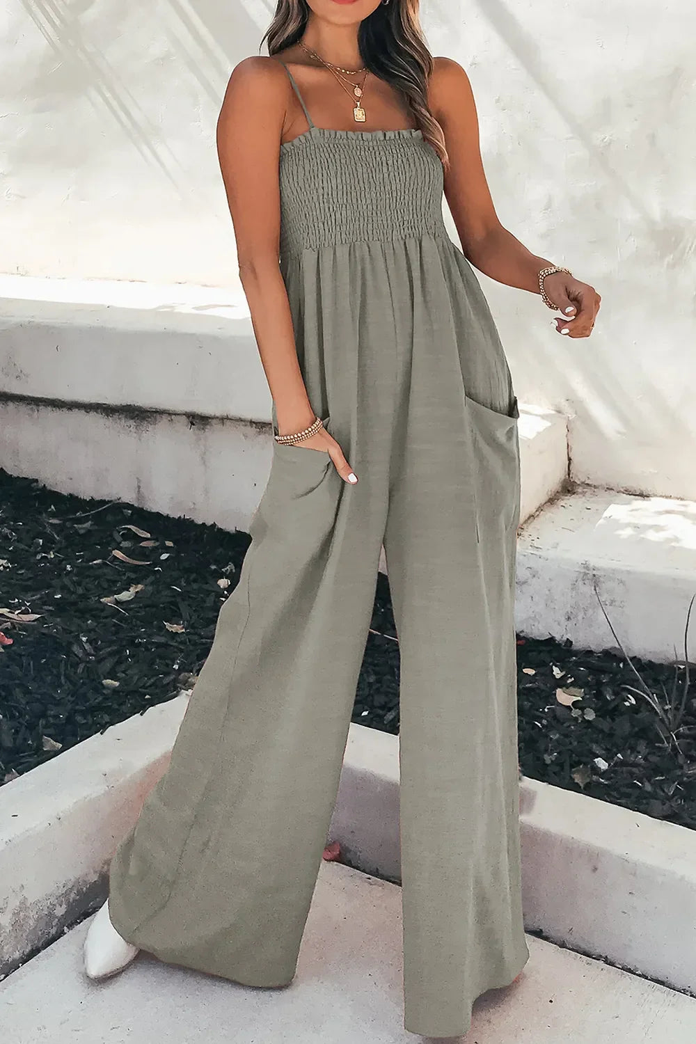 Woman wearing olive green smocked bodice wide-leg jumpsuit with spaghetti straps and pockets