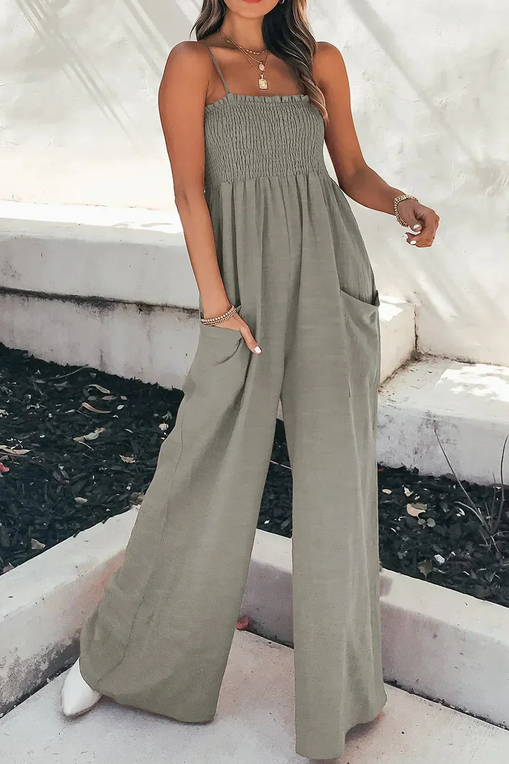 Woman wearing olive green smocked bodice wide-leg jumpsuit with spaghetti straps and pockets