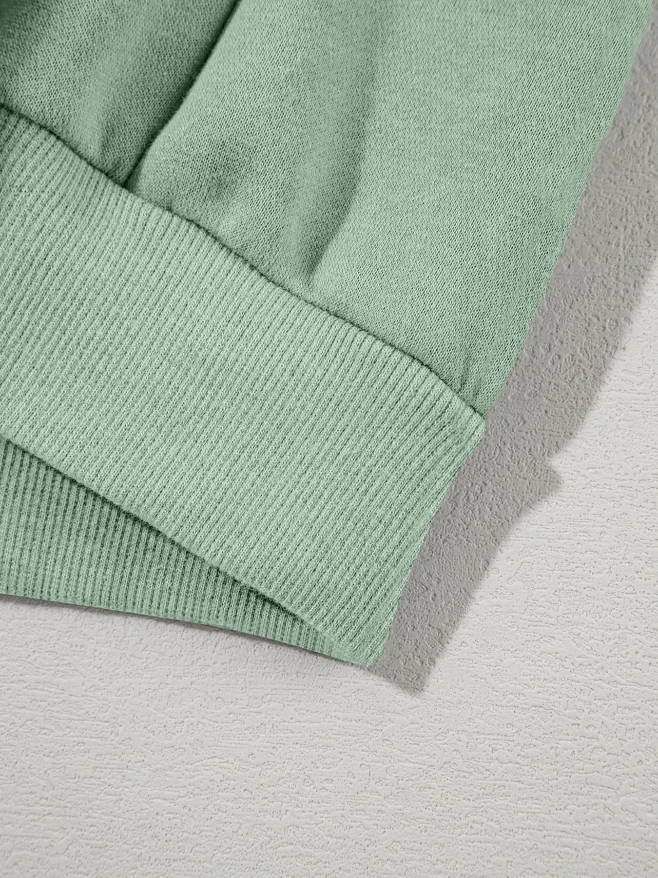 Close-up of mint green sweatshirt sleeve with ribbed cuff on textured light surface