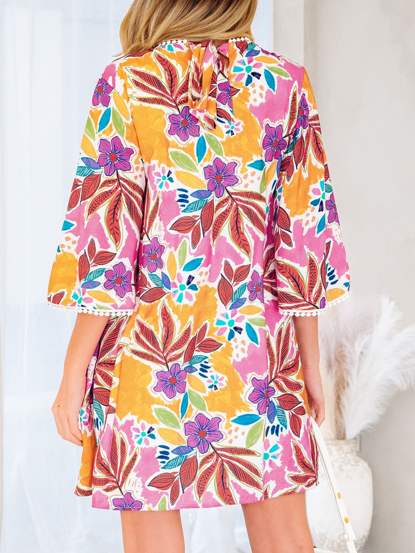 Woman wearing colorful floral print dress with bell sleeves and tie-back detail