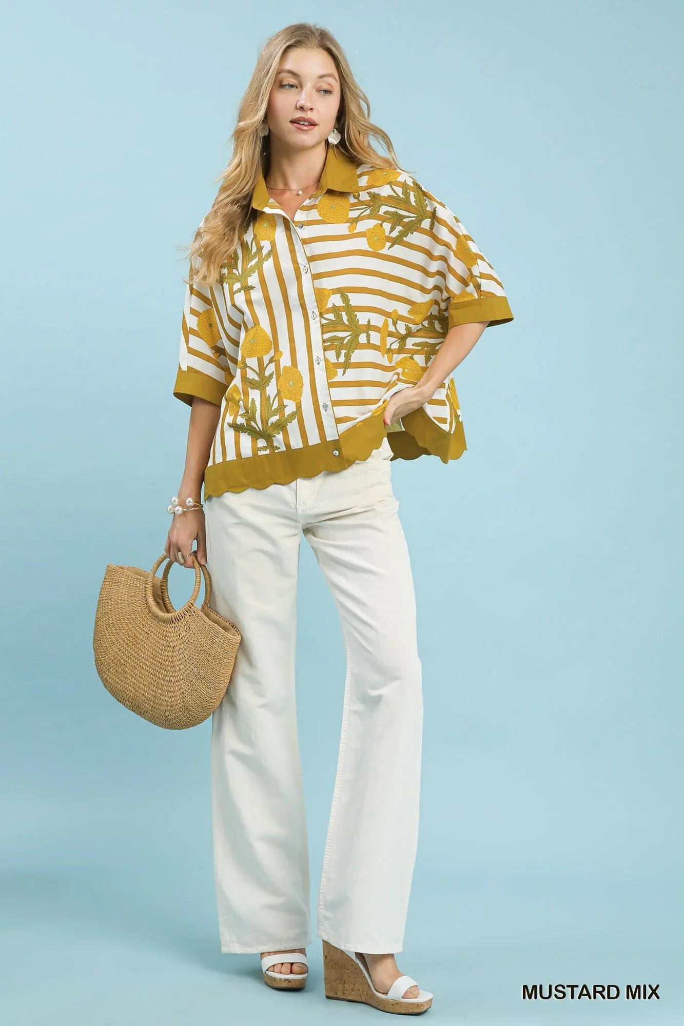 Woman in mustard yellow striped floral blouse, white wide-leg pants, holding straw bag