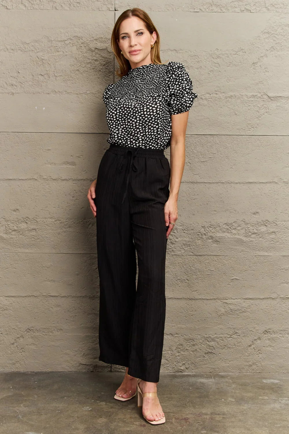 Woman wearing a black and white patterned blouse with short sleeves and high-waisted black pants