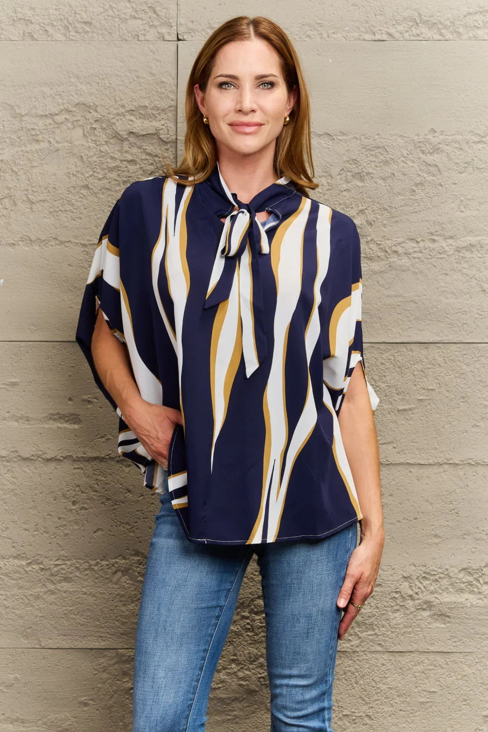 Woman wearing navy blue, white, and gold striped blouse with tie neck and blue jeans
