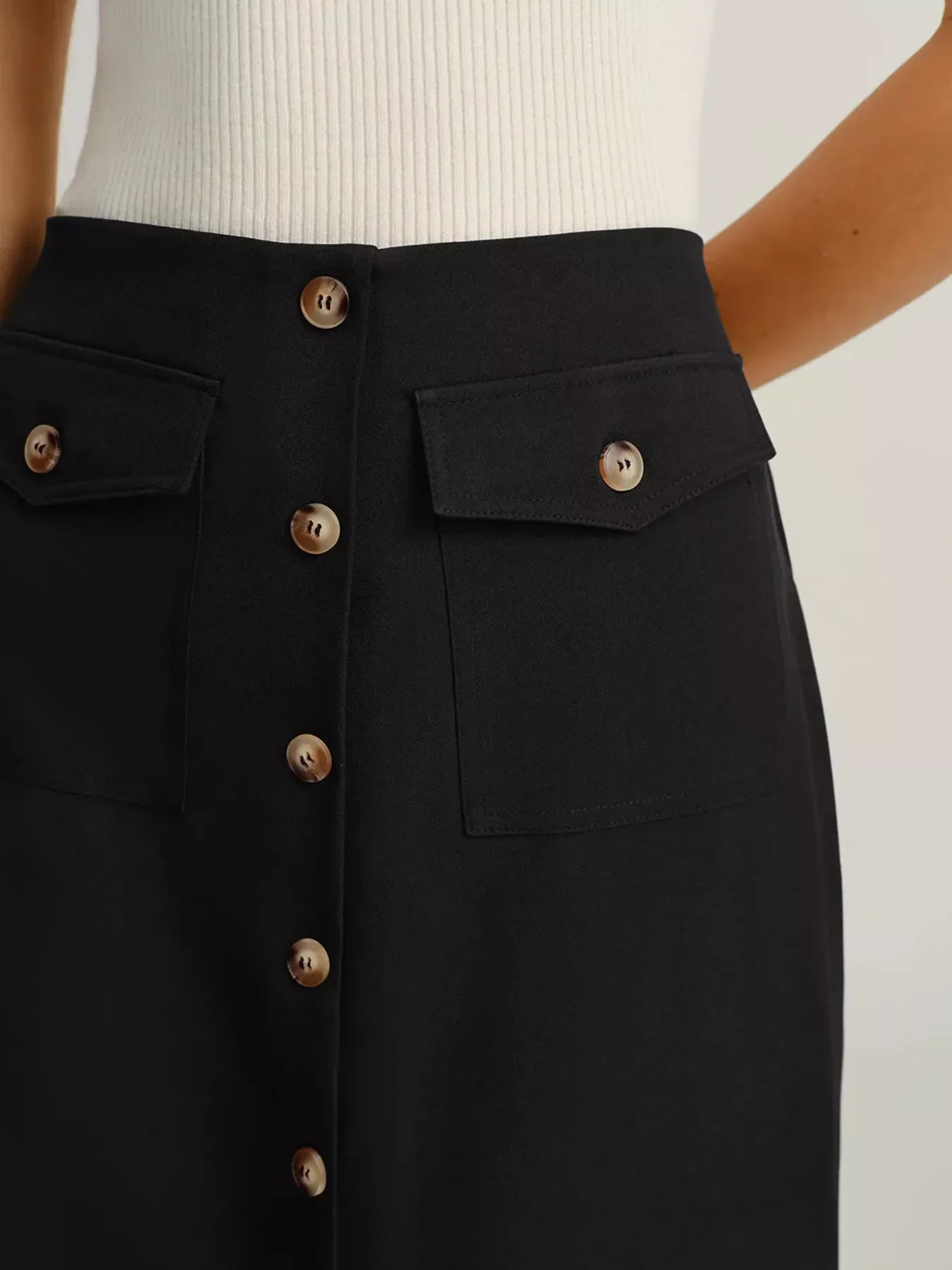 Close-up of black button-front skirt with flap pockets worn with white ribbed top