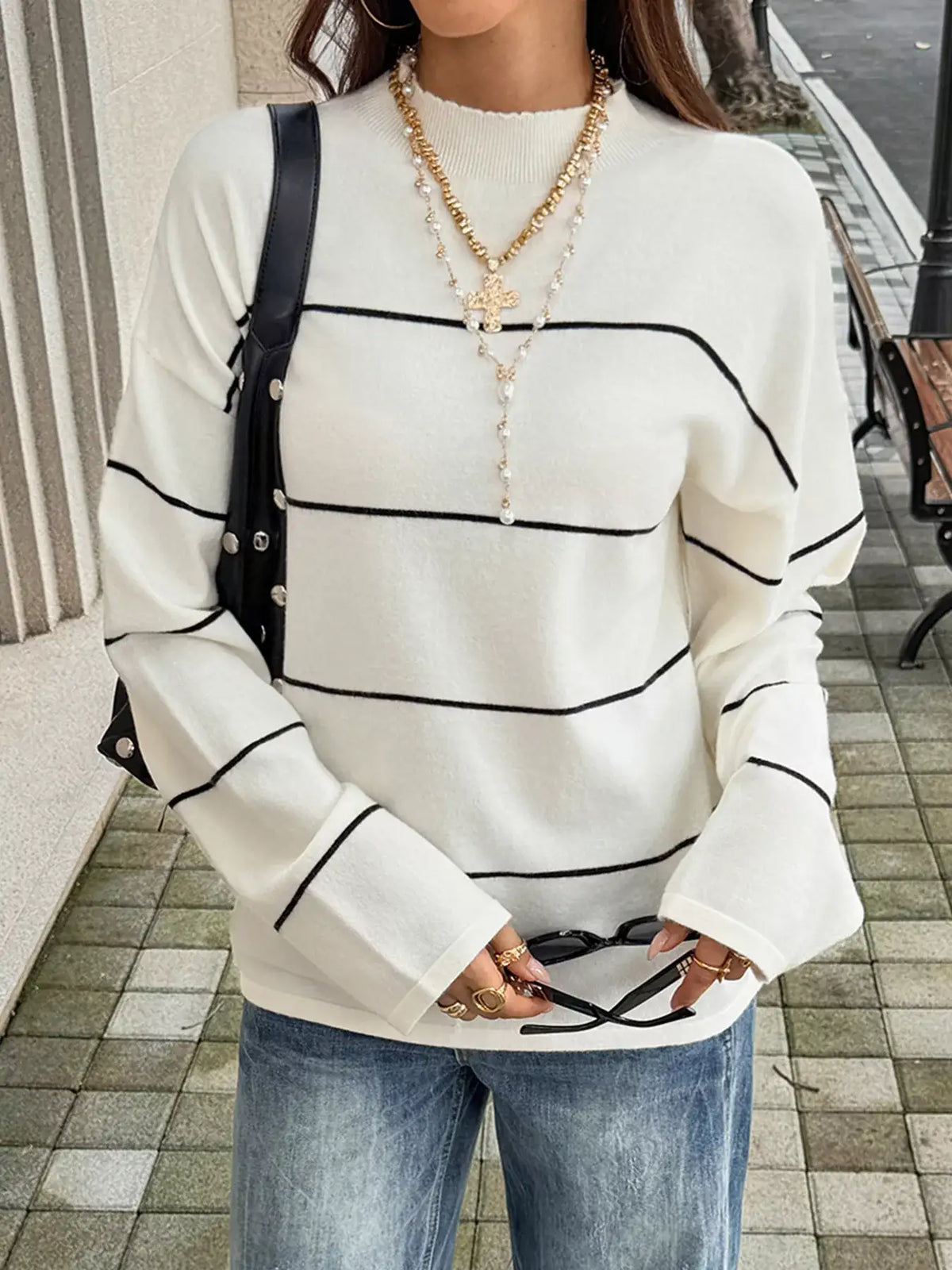 Woman wearing an Evie's Dreamland white striped mock neck sweater with long sleeves and blue jeans.