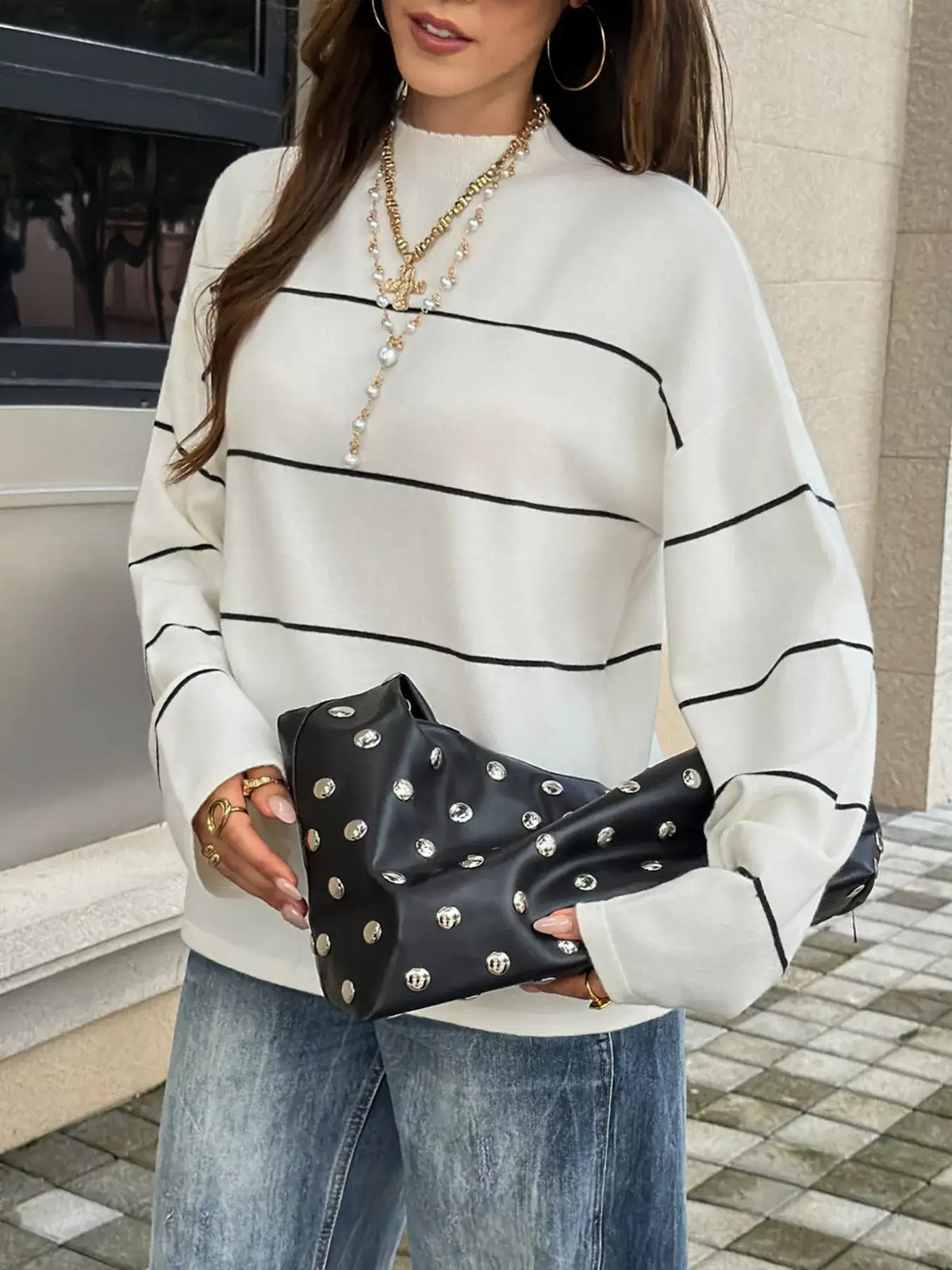 Woman wearing an Evie's Dreamland white striped mock neck sweater with a black studded clutch bag.