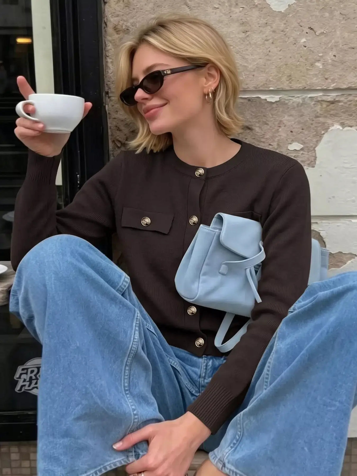 Woman wearing an Evie's Dreamland brown button-down knit cardigan with gold buttons and blue jeans.