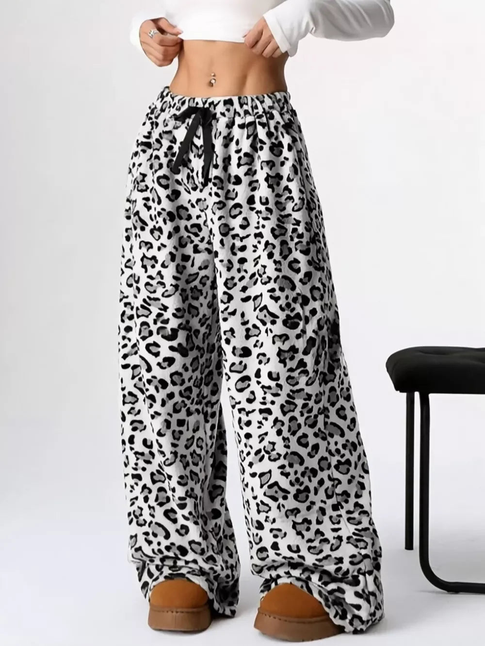 Woman wearing white and black leopard print wide-leg pants with a black drawstring, paired with brown slippers