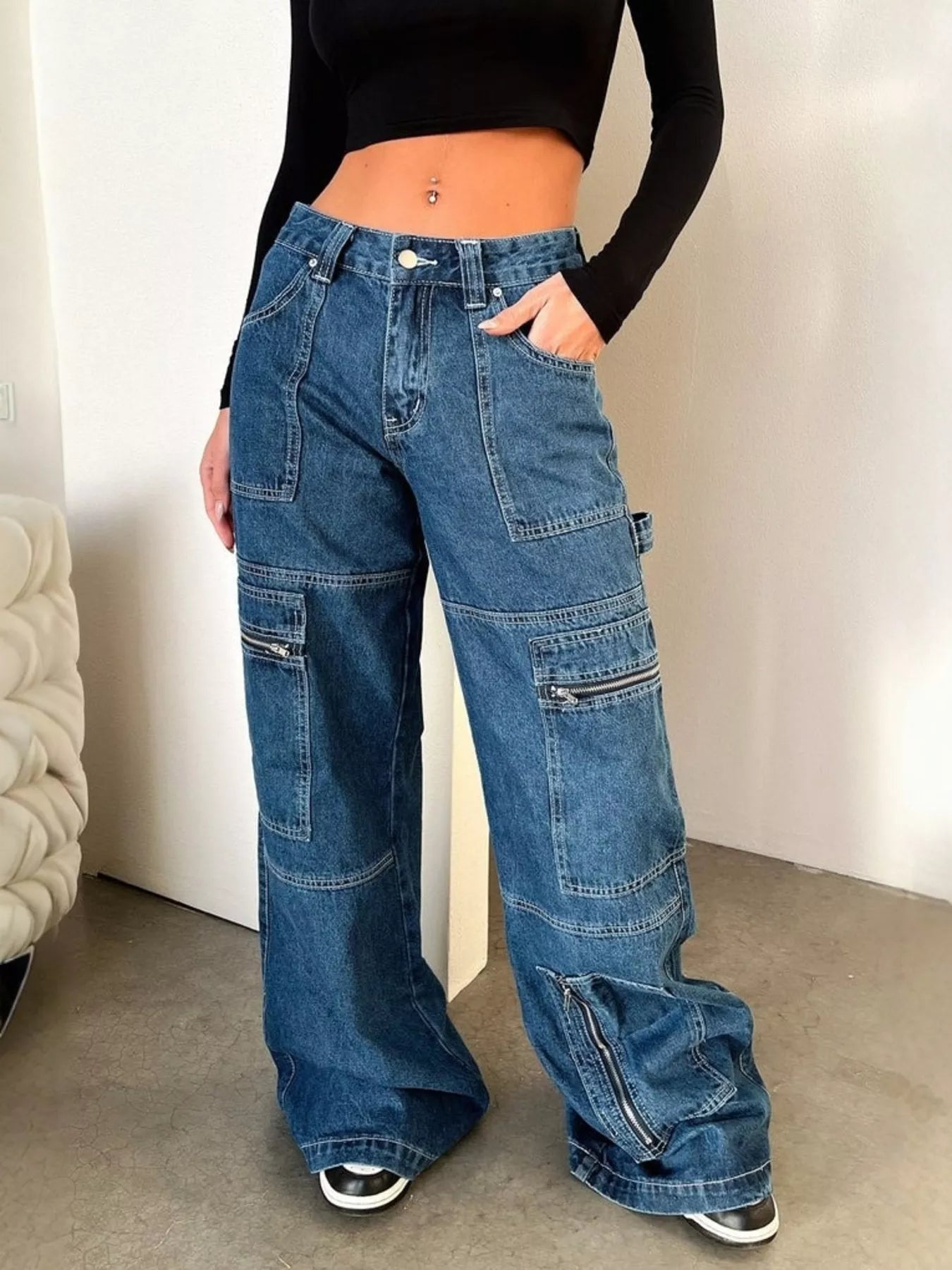 Woman wearing wide-leg denim cargo jeans with multiple pockets and a black crop top indoors.
