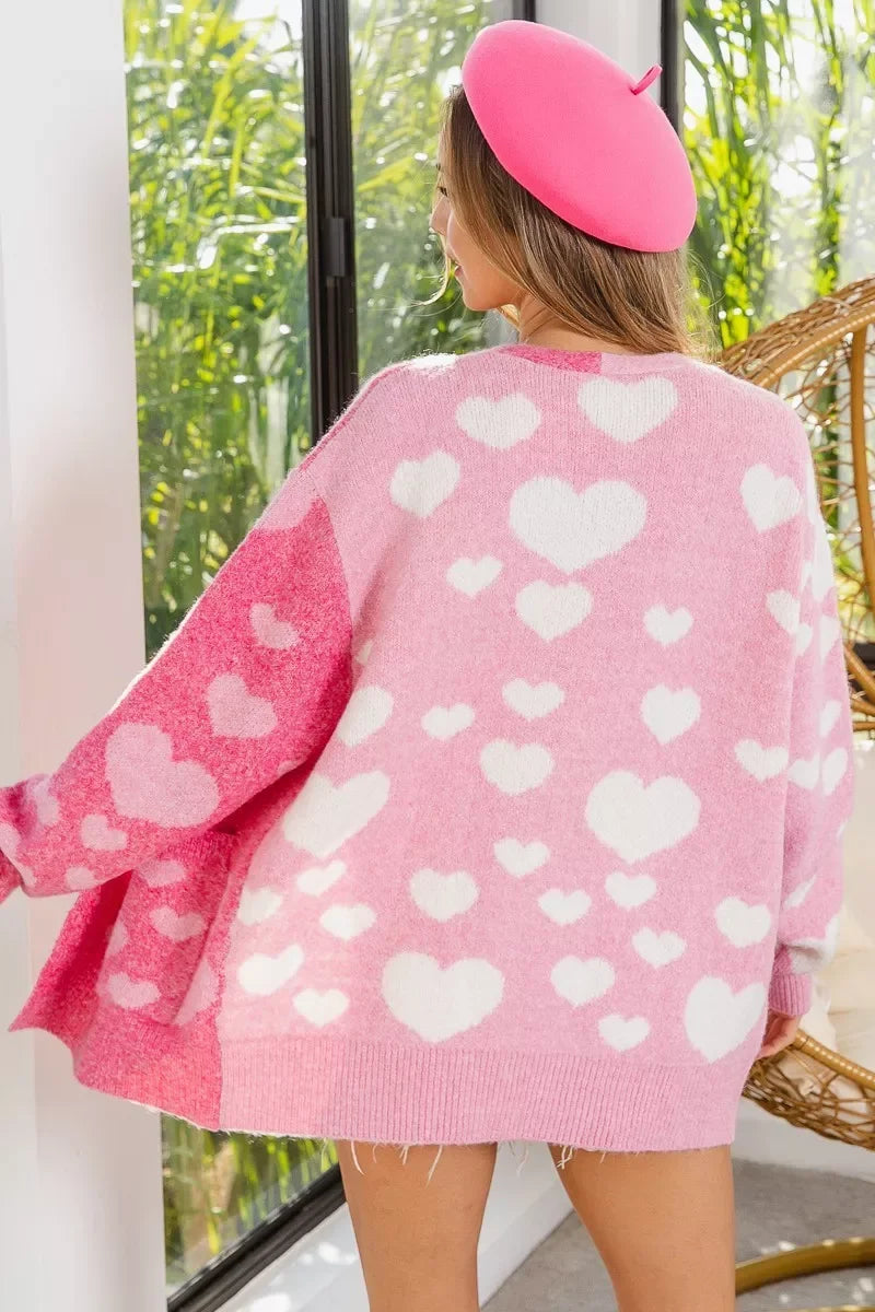 Woman wearing oversized pink heart-patterned sweater and pink beret indoors by window with green plants