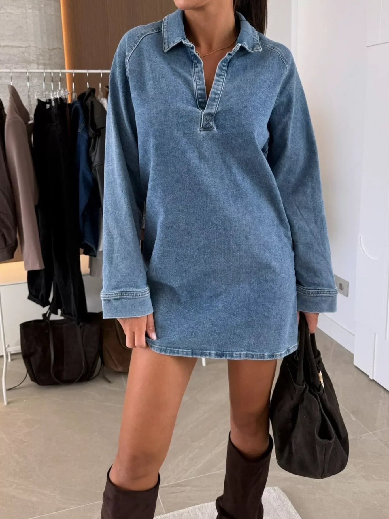 Woman in a denim shirt dress with long sleeves, knee-high boots, and a black handbag.