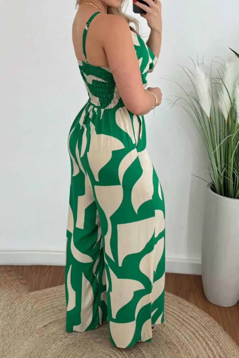 Woman wearing green and beige abstract print wide-leg jumpsuit posing indoors by a plant
