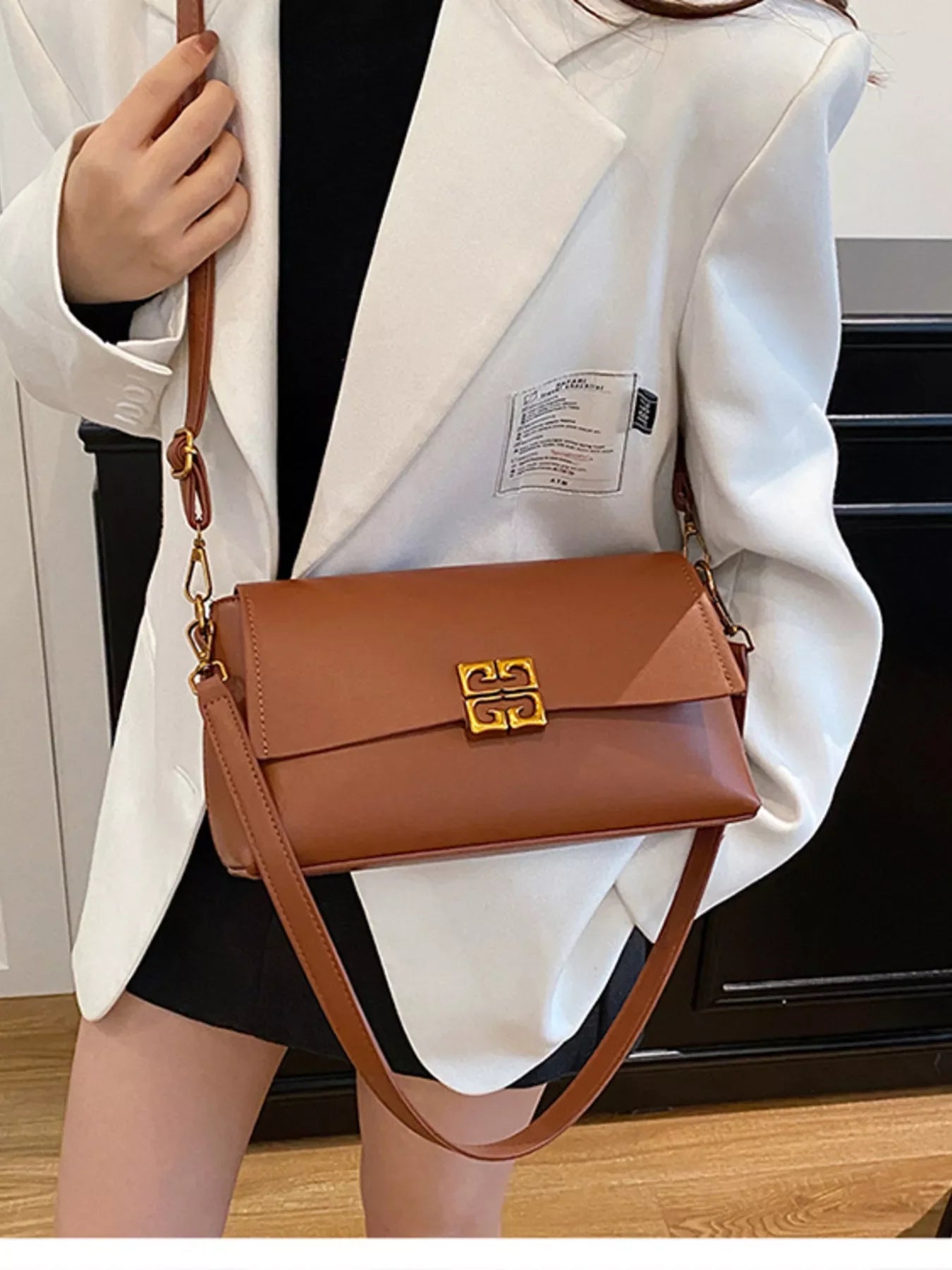 Woman wearing white blazer and black dress holding brown leather shoulder bag with gold clasp