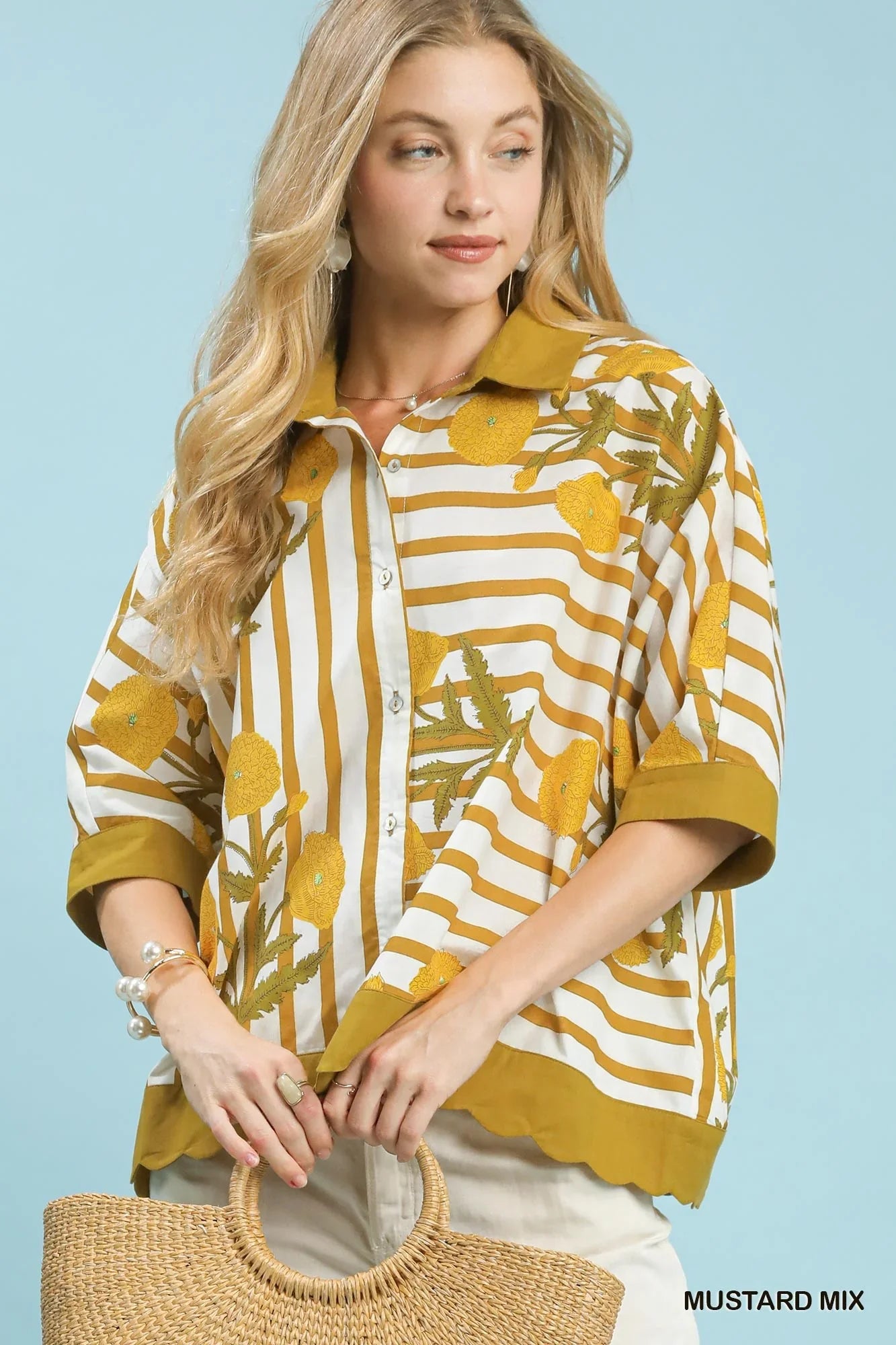 Woman wearing a mustard yellow striped floral button-up blouse, holding a woven bag